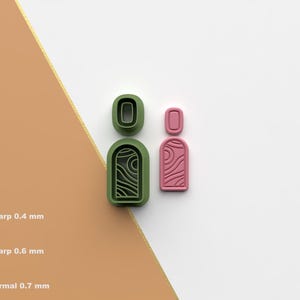 May include: A set of three earring-shaped cookie cutters in green and pink. The green cutters have a wavy design, while the pink one has a swirl pattern. The image also shows the STL file icon and the text "Sharp 0.4 mm", "Sharp 0.6 mm", and "Normal 0.7 mm".