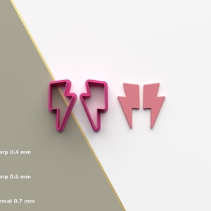 May include: Two pink lightning bolt cookie cutters, one with a single bolt and the other with two bolts facing opposite directions. The cutters are on a white surface.