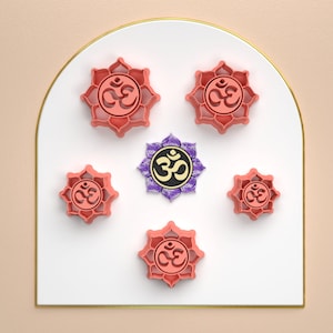 May include: Six pink lotus flower charms with an Om symbol in the center. The charms are arranged in a circle on a white background with a gold border.