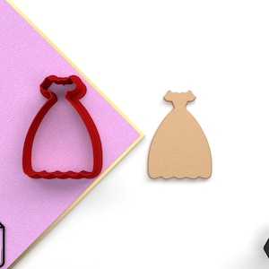 May include: Red plastic cookie cutter in the shape of a dress with a scalloped hem. The cutter is on a pink background. A brown plastic dress cookie cutter is on a white background.