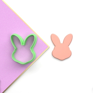 May include: A green plastic bunny cookie cutter and a pink plastic bunny cookie cutter. The cookie cutters are on a white background.