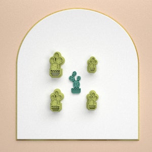 Puede incluir: Cinco cortadores de galletas de cactus verdes sobre un fondo blanco. Los cortadores de galletas de cactus son de diferentes formas y tamaños.
