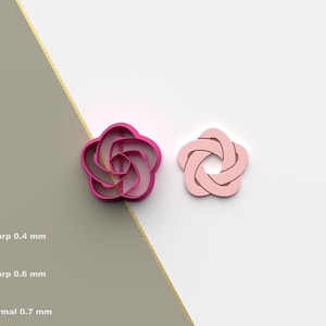 May include: Two pink 3D printed cookie cutters in the shape of a flower. The cutter on the left is a darker pink and the cutter on the right is a lighter pink.