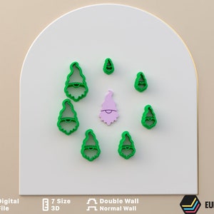 Puede incluir: Siete cortadores de galletas de plástico verde con forma de gnomos con diferentes expresiones faciales. Los cortadores están dispuestos en círculo sobre una superficie blanca. El texto "7 Size 3D" y "Double Wall Normal Wall" es visible debajo de los cortadores.