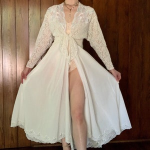May include: A white lace robe with a long, flowing skirt and a lace overlay. The robe has a V-neckline and a tie at the waist.