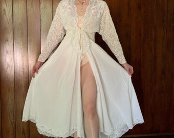 May include: A white lace robe with a long, flowing skirt and a lace overlay. The robe has a V-neckline and a tie at the waist.