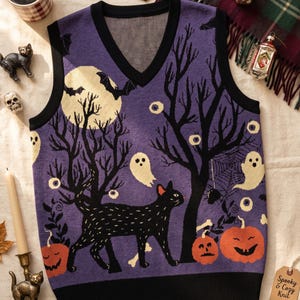 May include: A purple V-neck sweater vest featuring a black cat, orange pumpkins, white ghosts, a full moon, and bare trees. The knit garment has black trim at the neckline and hem. A small brown tag attached to the side reads Spooky & Cozy Knit.