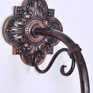 May include: Ornate bronze wall sconce with a decorative floral design. The sconce features a curved arm and a decorative backplate with intricate detailing. The fixture is mounted on a white wall.
