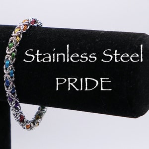 May include: Stainless steel bracelet with a rainbow colored chain. The bracelet is on a black display stand with the words "Stainless Steel Pride" written in white.