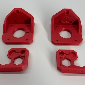 May include: Four red 3D printed plastic parts for a 3D printer. Two of the parts are larger and have a circular opening in the centre. The other two parts are smaller and have two circular openings.