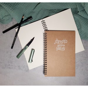 thoughts become reality | handbeschriebenes A5-Notizbuch mit Spruch | weiße Schrift | Kraftpapiercover | 100 Blätter | Spiralbindung