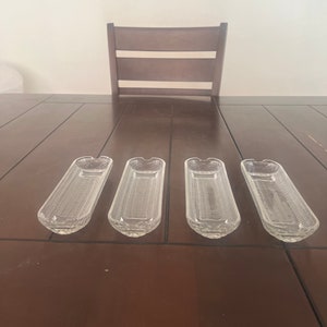 May include: Four clear glass serving dishes with a ribbed pattern. The dishes are arranged in a row on a wooden table.