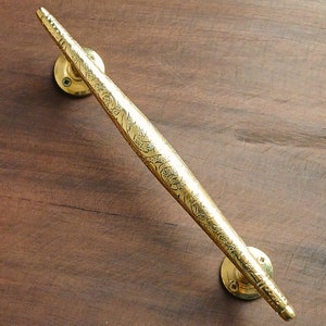 Puede incluir: Una manilla de puerta dorada con un diseño ornamentado. La manilla es larga y delgada con un extremo puntiagudo.