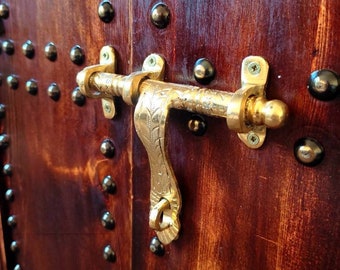 May include: A close-up of a wooden door with a brass latch. The door is decorated with a pattern of metal studs.