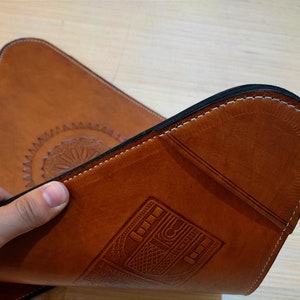 May include: A brown leather desk mat with a decorative design and a stitched edge. The mat has a vintage radio design embossed into the leather.