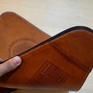 May include: A brown leather desk mat with a decorative design and a stitched edge. The mat has a vintage radio design embossed into the leather.