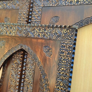 May include: Close-up of intricately carved wooden panels. The panels feature detailed geometric and floral patterns, with a dark brown finish. The carvings are highlighted with a contrasting blue color, adding depth and visual interest to the artwork.
