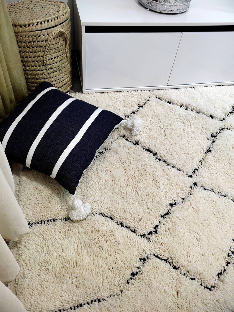May include: A white shag rug with a black diamond pattern. The rug is in a room with a white cabinet and a black and white striped pillow.
