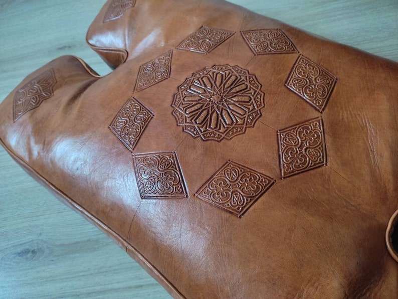 May include: A brown leather pouf with intricate embossed diamond patterns and a central circular design.
