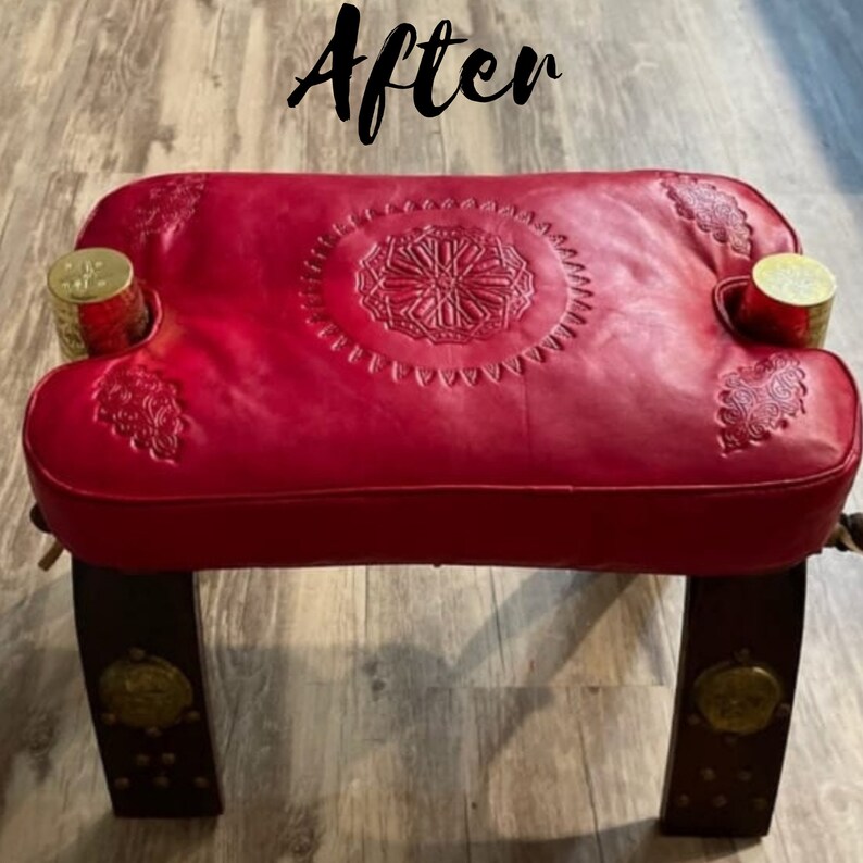 May include: A red leather ottoman with a decorative embossed pattern and gold metal accents. The ottoman has two legs and is made of wood.