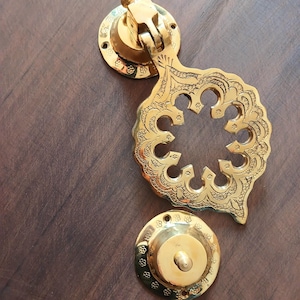 Può includere: Un batacchio per porta dorato con intricati disegni floreali. Il batacchio ha una base rotonda e un'impugnatura decorativa con un puntale appuntito.