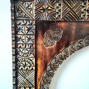 May include: A dark brown wooden frame with intricate carvings. The frame has a rounded arch at the top and a geometric pattern around the edges.