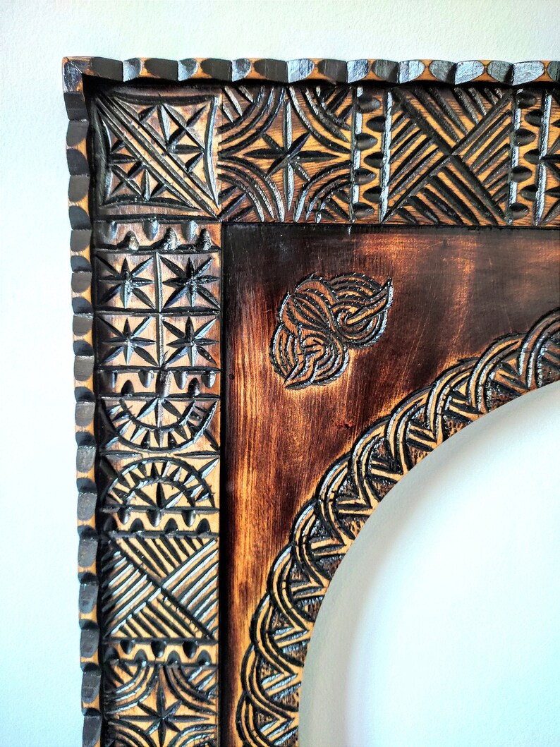 May include: A dark brown wooden frame with intricate carvings. The frame has a rounded arch at the top and a geometric pattern around the edges.