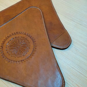 May include: Two brown leather triangular coasters with decorative stitching around the edges. One coaster features a circular design with intricate details.