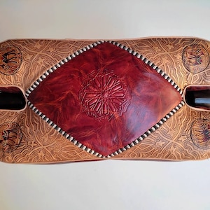 May include: A red leather ottoman with intricate embossed patterns and a diamond-shaped center panel. The ottoman has a wooden base and is decorated with a traditional Moroccan design.