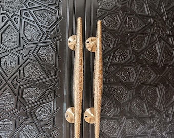 May include: Close-up of a black door with a geometric pattern and two gold-colored, ornate door handles. The handles are vertically aligned and feature intricate designs, adding a touch of elegance to the door's aesthetic.