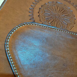 May include: Two brown leather coasters with a decorative stitched edge. The larger coaster has a detailed embossed design in the center.