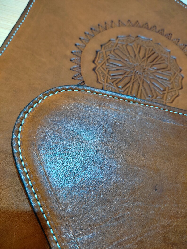 May include: Two brown leather coasters with a decorative stitched edge. The larger coaster has a detailed embossed design in the center.