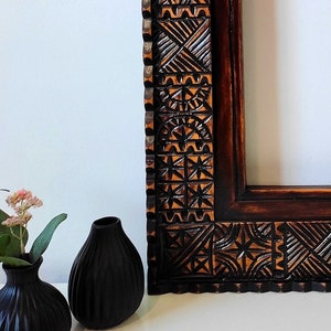 May include: A dark brown wooden picture frame with intricate carved designs. The frame has a scalloped edge and is made of a dark wood with a reddish hue.