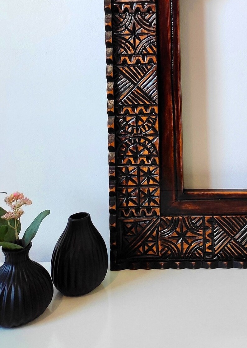 May include: A dark brown wooden picture frame with intricate carved designs. The frame has a scalloped edge and is made of a dark wood with a reddish hue.