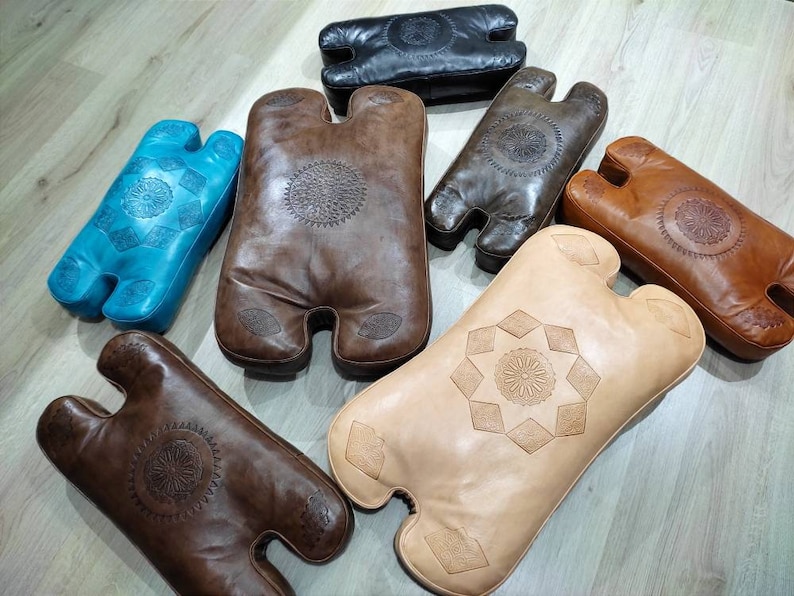 May include: Assortment of six leather cushions in various colors and patterns. The cushions are all in the shape of a human torso with two arms. The cushions are made of leather and have intricate designs.
