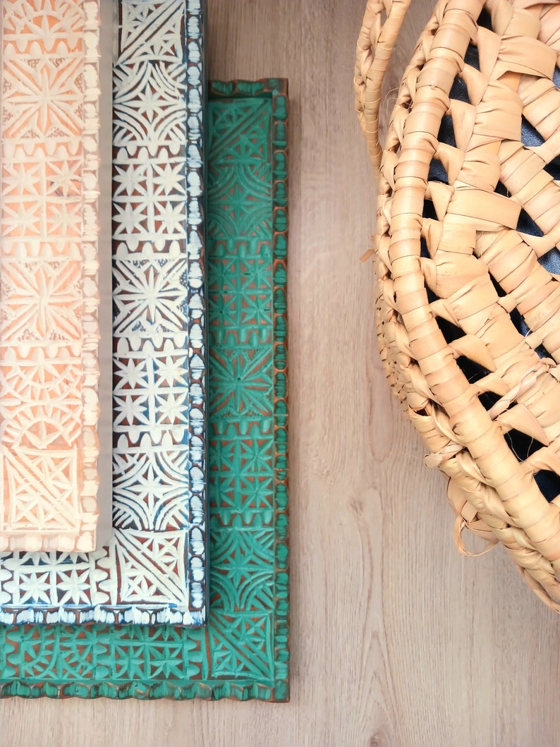 May include: Three decorative wooden trays with intricate geometric patterns. The top tray is peach, the middle tray is white with blue accents, and the bottom tray is green. The trays are stacked on top of each other.