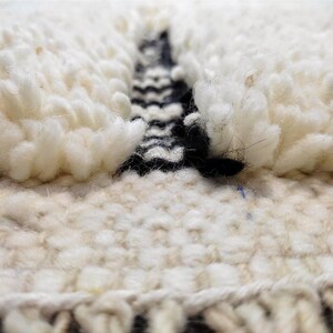 May include: Close-up of a white and black woven rug with a textured, fluffy surface. The rug has a geometric pattern in black and white.