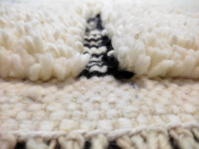May include: Close-up of a white and black woven rug with a textured, fluffy surface. The rug has a geometric pattern in black and white.