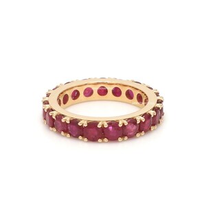 May include: A gold band ring with a row of red ruby stones.
