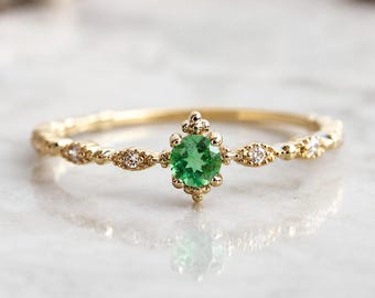 Puede incluir: Un anillo de oro con una piedra preciosa verde redonda en el centro rodeada de pequeñas cuentas doradas. La banda está decorada con cuatro pequeñas piedras transparentes en engastes dorados con forma de marquesa, creando una joya detallada.