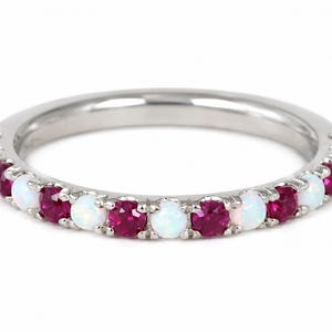 May include: A silver-toned metal band ring featuring an alternating pattern of round, iridescent white opals and vibrant, deep pinkish-red rubies set in a shared-prong style along the front half of the circular band, creating a continuous row.