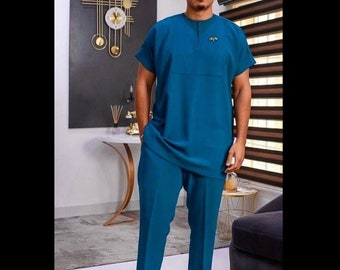 May include: A teal blue two-piece outfit with a short-sleeved collared shirt and matching pants. The shirt has a small gold pin on the front.