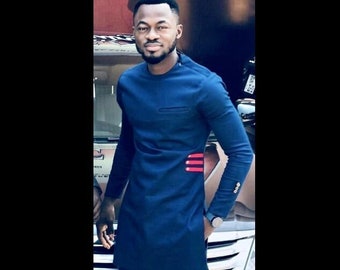 May include: A man wearing a dark blue long-sleeved shirt with a red and white design on the side. He is also wearing dark blue pants and black shoes.