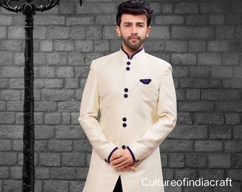 Pode incluir: Uma kurta de manga comprida de cor creme com colar mandarim e uma fila de botões pretos. A kurta tem uma borda azul em torno do colar e dos punhos. O modelo está vestindo a kurta com uma calça azul escura.