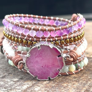May include: A multi-layered bracelet with brown leather cord, amethyst beads, gold beads, and a large pink agate stone in the center.