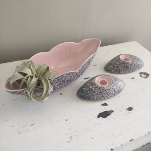 Puede incluir: Un conjunto de tres piezas de cerámica vintage en un patrón moteado rosa y negro. El conjunto incluye un tazón grande con forma de hoja y dos candelabros más pequeños.
