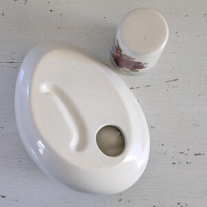 May include: White ceramic dish with a round hole in the center and a raised edge. The dish has the words "Made in Japan" printed on the bottom. A smaller white ceramic cup with a floral design is next to the dish.