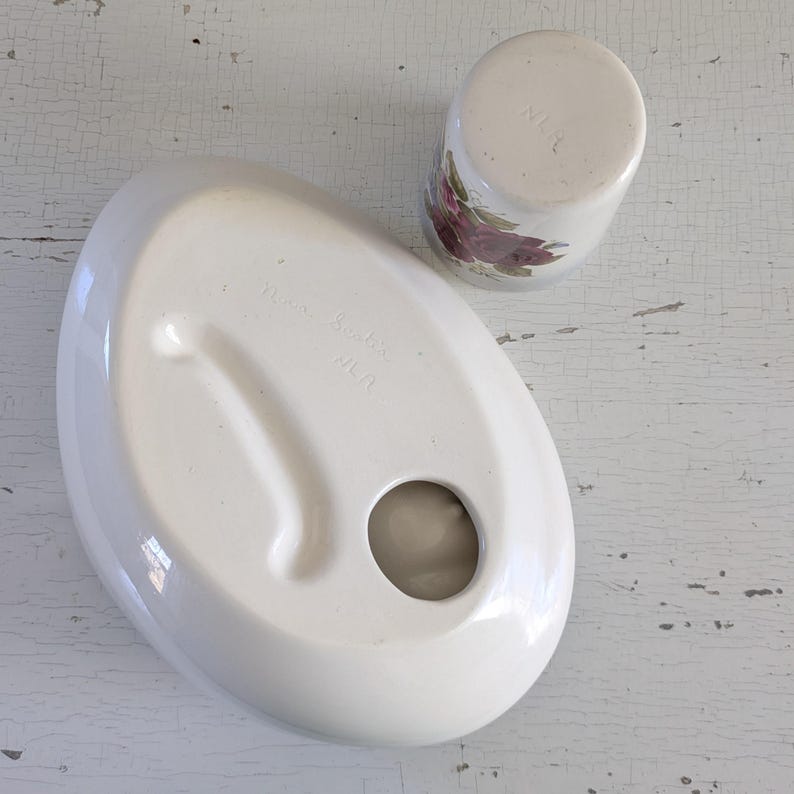 May include: White ceramic dish with a round hole in the center and a raised edge. The dish has the words "Made in Japan" printed on the bottom. A smaller white ceramic cup with a floral design is next to the dish.