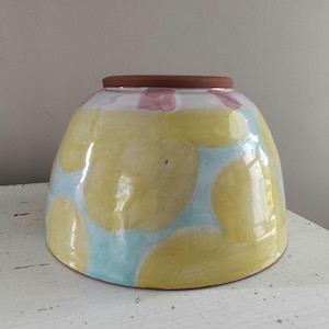 May include: A large, yellow ceramic bowl with a blue and white pattern. The bowl has a brown rim and is glazed.