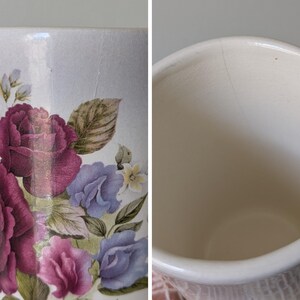 May include: A white ceramic mug with a floral design featuring pink and purple roses, blue flowers, and green leaves. The mug has a crack on the side.